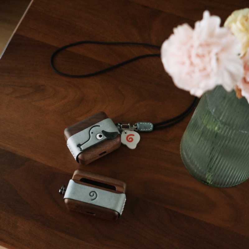 Cute Doggy AirPods Pro Case Wood Walnut Leather iwoodstore Two wooden camera-shaped objects on a wooden surface with a vase of flowers in the background.