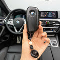 Hand holding a BMW key fob with a beaded chain against a light gray background