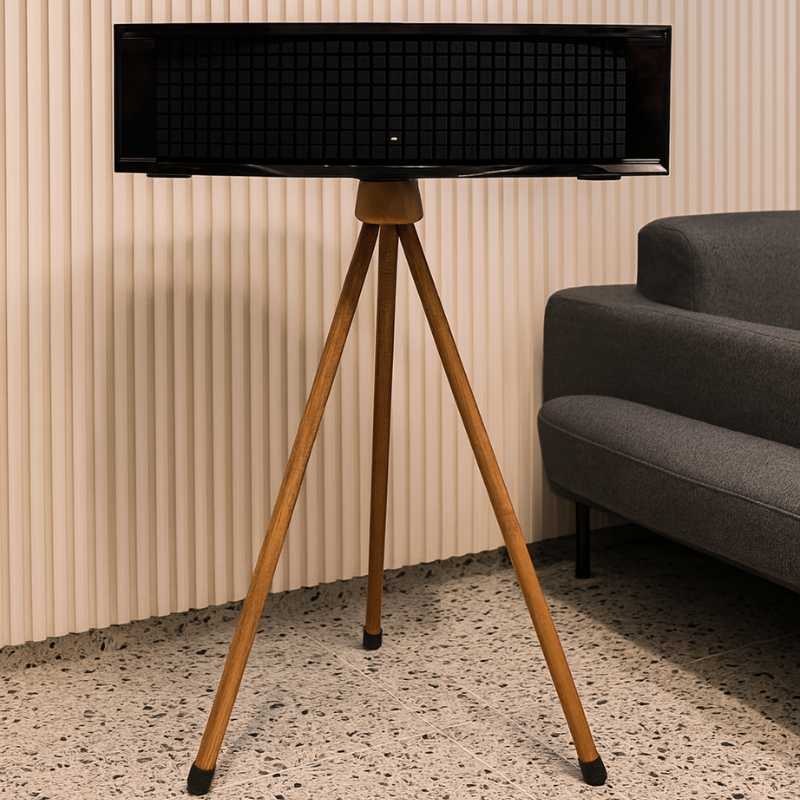 JBL L75MS Stand Holder Wood Tripod - iWoodStore Black speaker on a wooden tripod stand in a room with a gray sofa and striped wall.