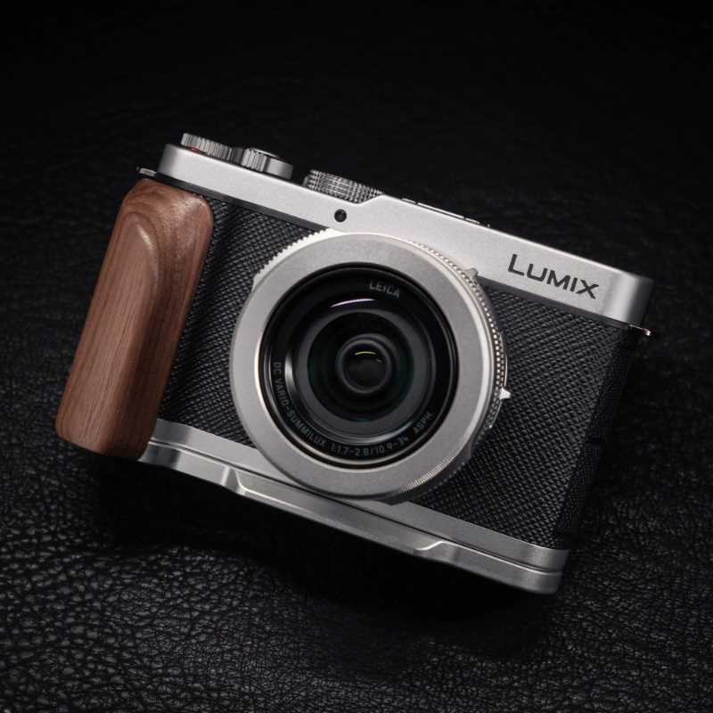 Panasonic Lumix compact camera with a silver body, black textured grip, and a brown wooden handle, shown on a dark textured background.