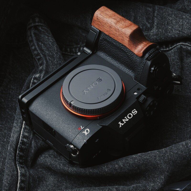A Sony Alpha camera with a wooden handle grip and black mounting bracket, resting on dark gray denim fabric.