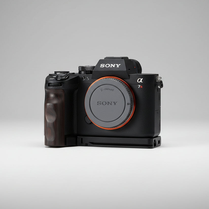Sony Alpha 7R camera body with a black grip attachment and an orange accent ring around the lens protector, resting on a dark gray textured fabric background.