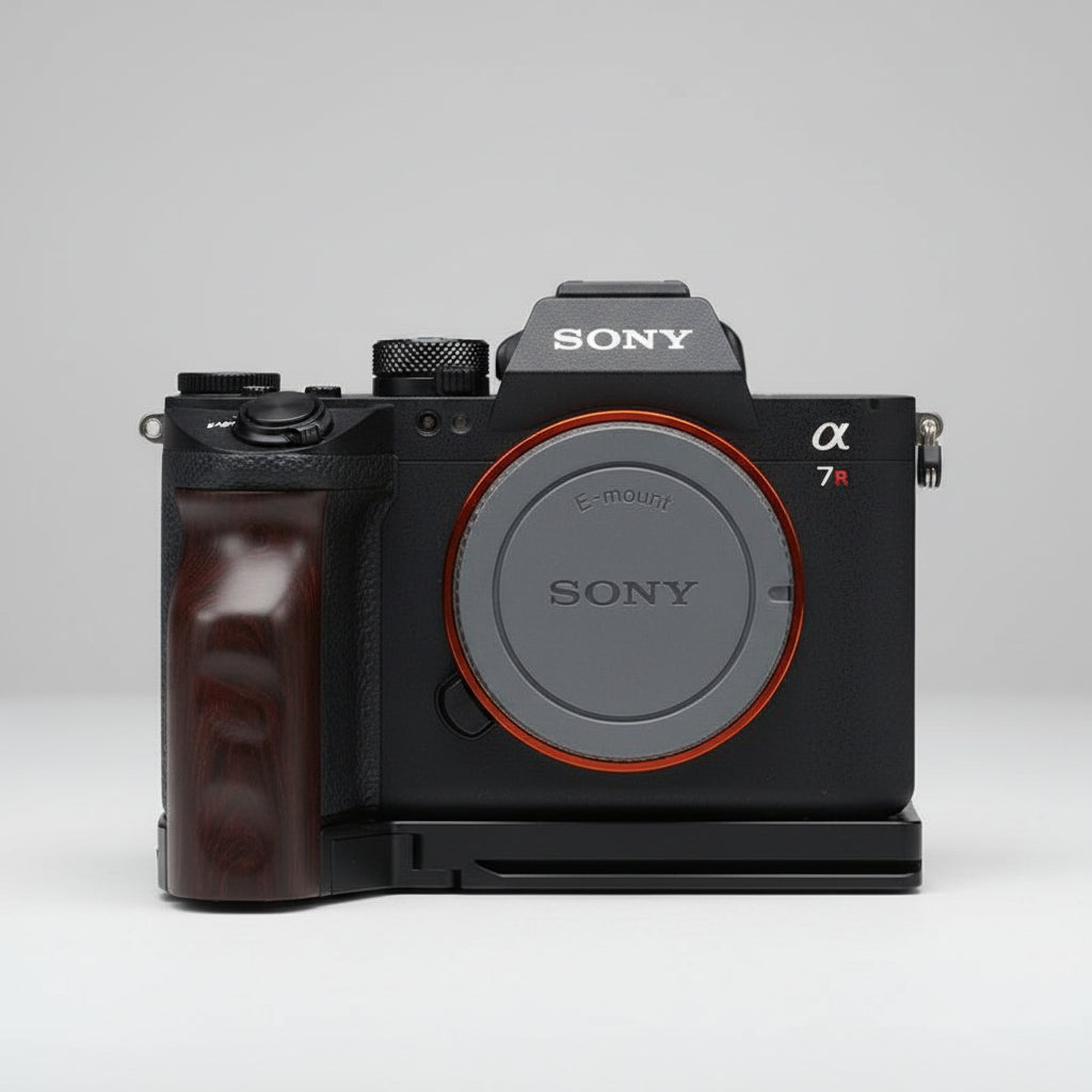 Sony Alpha 7R camera body with a black grip attachment and a black lens cap with an orange ring, resting on a dark gray textured fabric background.