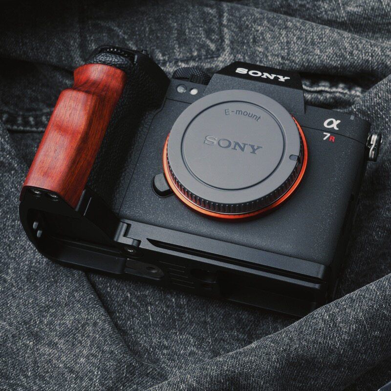 Sony Alpha 7R camera body with a black grip featuring a reddish-brown wood inlay, resting on a dark gray textured fabric background.
