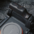 A close-up of a Sony mirrorless camera body fitted with a dark brown wooden handgrip, resting on a textured gray denim background.