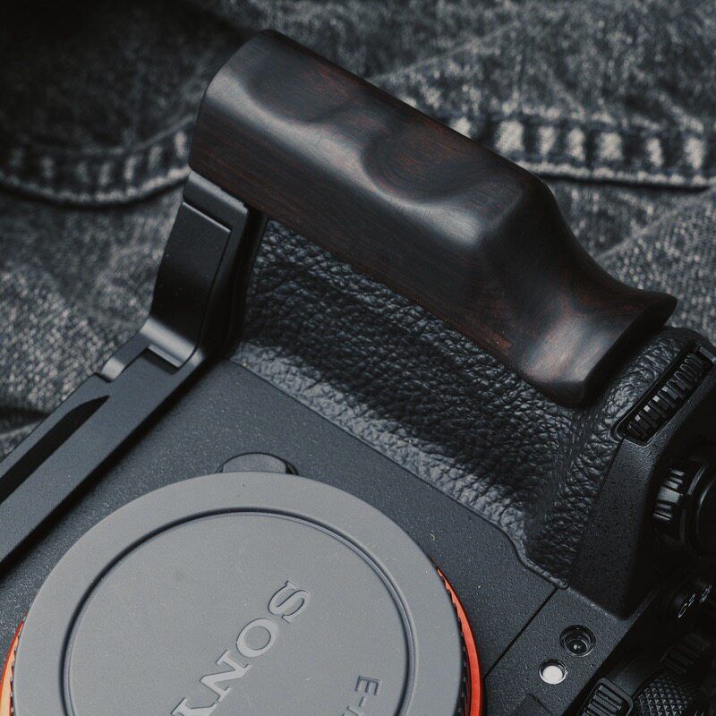 A close-up of a Sony mirrorless camera body fitted with a dark brown wooden handgrip, resting on a textured gray denim background.