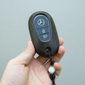 Hand holding a Mercedes-Benz key fob with a gray background